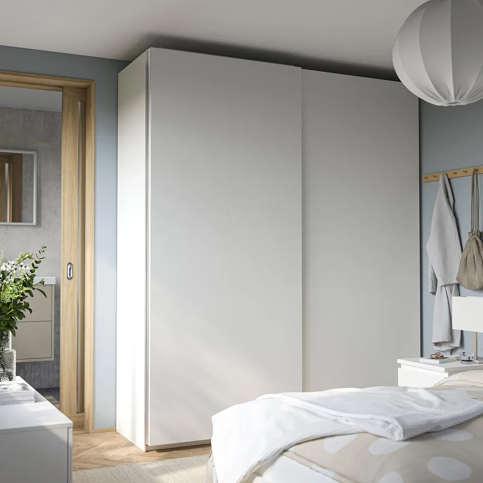 Bedroom with large grey PAX wardrobe, sliding doors, white bed, and mirror. Minimalist design, light wood floors.