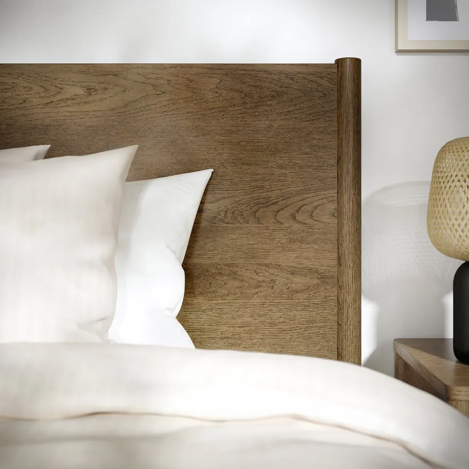 Luxurious wooden bed with plush white pillows & woven bedside lamp, focusing on quality materials & sleek design.
