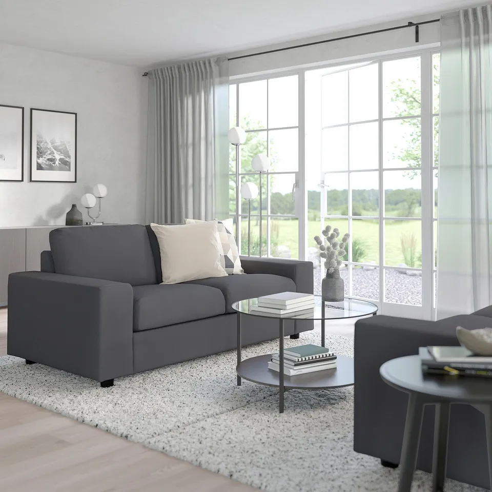 Modern living room with grey sofa, glass coffee table, and big windows.