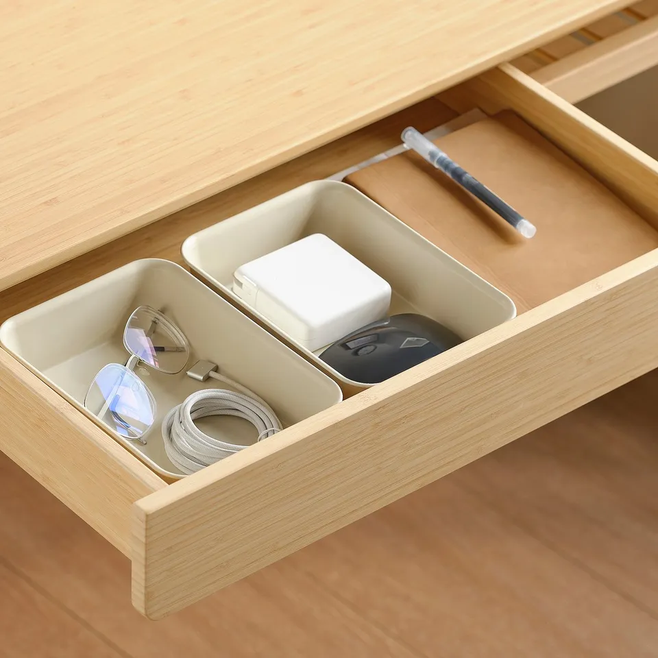 Organised desk drawer with compartments storing glasses, charger, adapter, and pens.