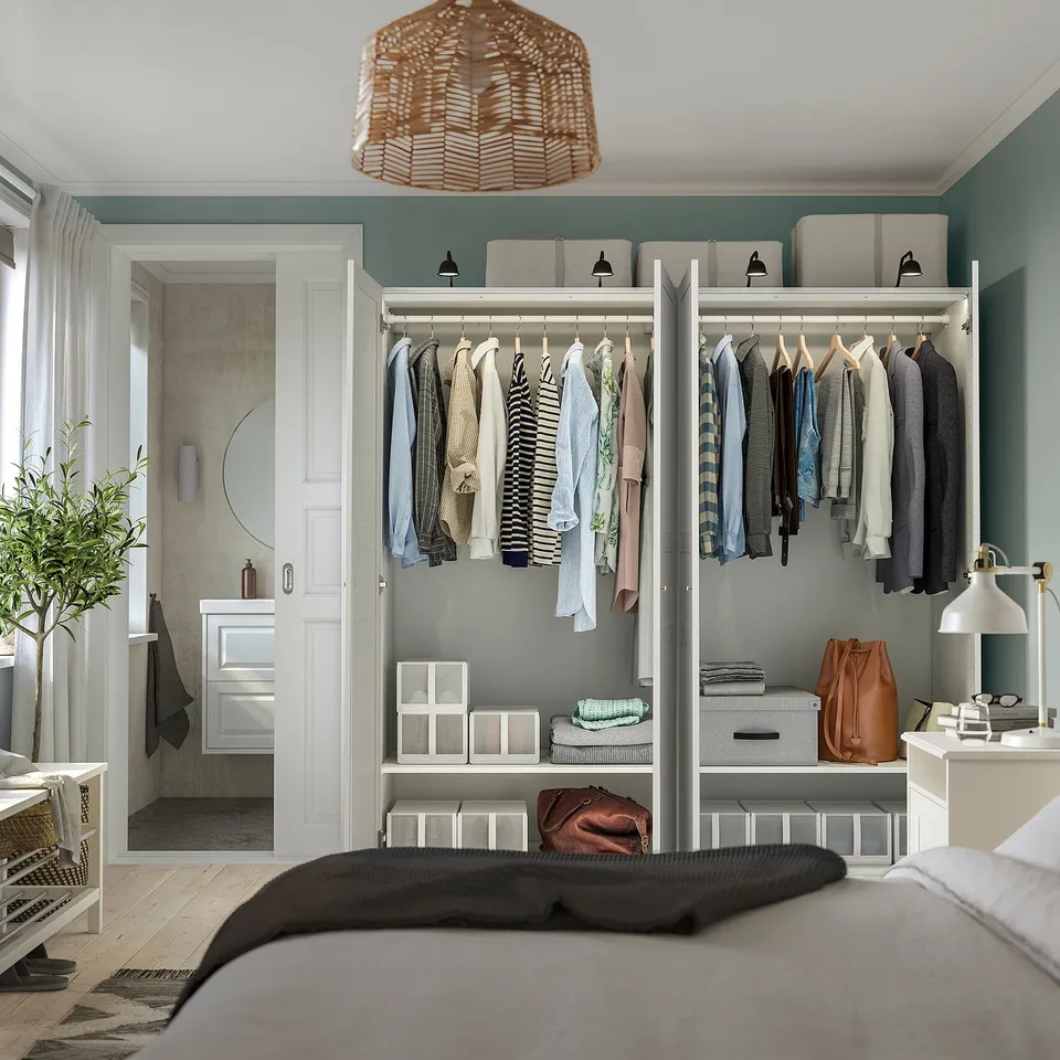 Well-organized bedroom featuring a PAX wardrobe system with clothes and storage boxes. Includes adjustable feet, dampened hinges, and a hanging plant.