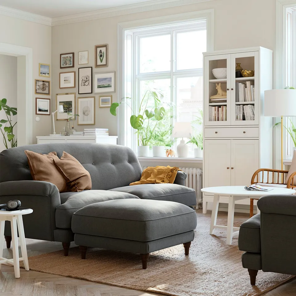 Living room with ESSEBODA footstool, cushions, and art near window.