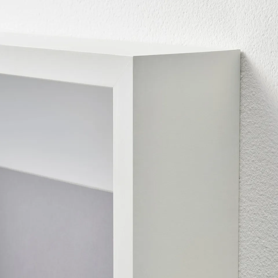 White SANNAHED picture frame with clear plastic front, mounted on a wall.