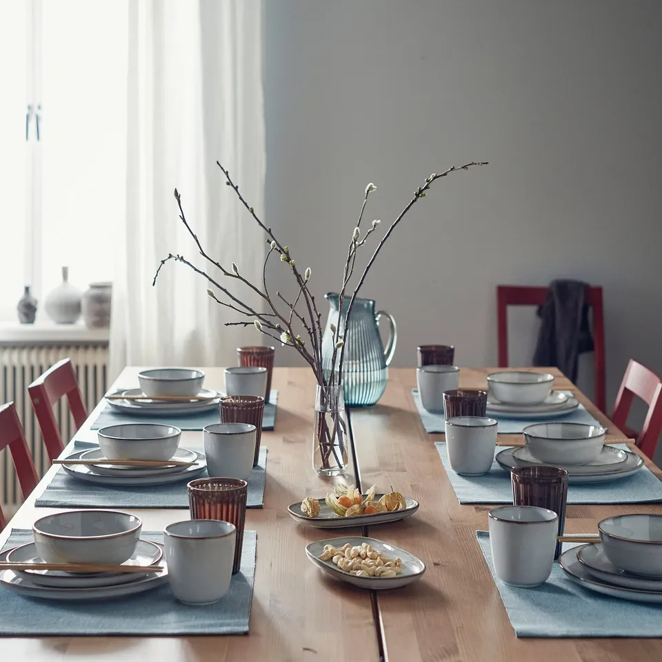 Table set with unique GLADELIG bowls, blue placemats, red chairs, and a floral centrepiece.