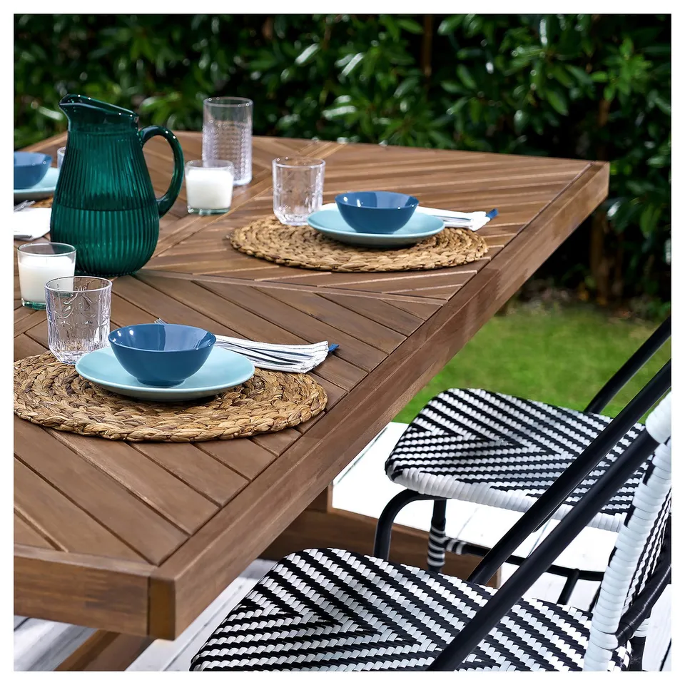 Outdoor table set with blue bowls, glasses, and teal jug on woven placemats; black and white chair.