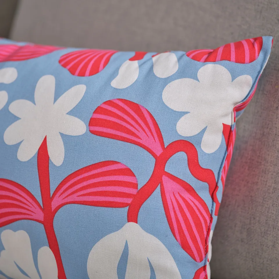 Small cushion with vibrant red and white flowers on light blue fabric, high quality and detailed pattern.