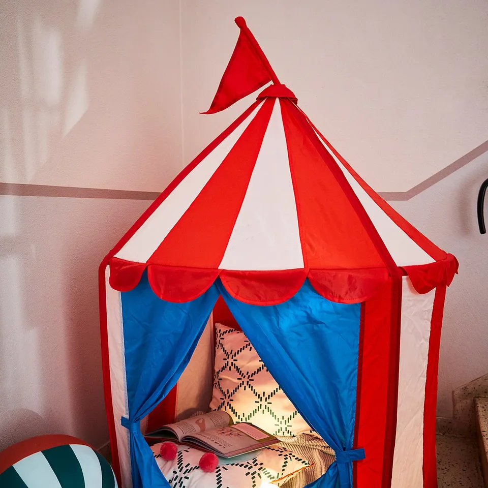 A red and white striped tent with blue lining, inside with colourful cushions and a small lamp.