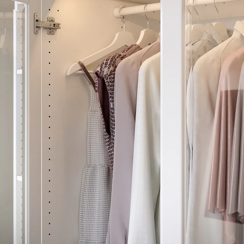 Organised closet with KOMPLEMENT white rail, hanging clothes in different shades of pink and white. Steel-made rail holds hangers neatly.