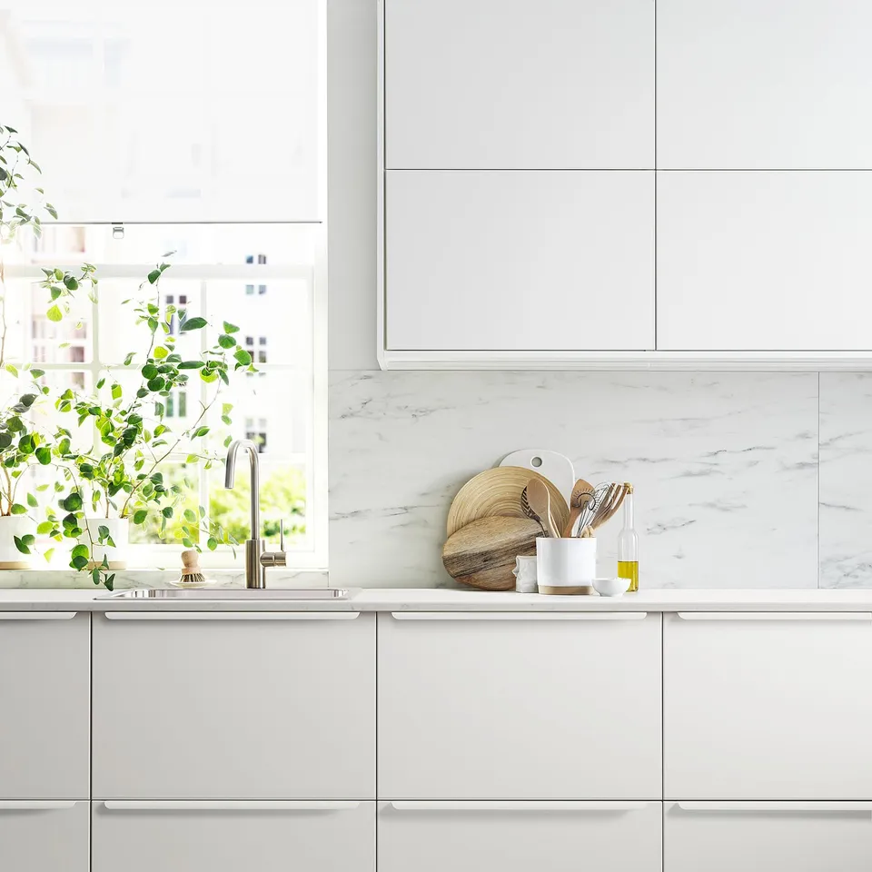 Modern white kitchen with marble countertop, sleek cabinetry, stainless tap, and potted plant.