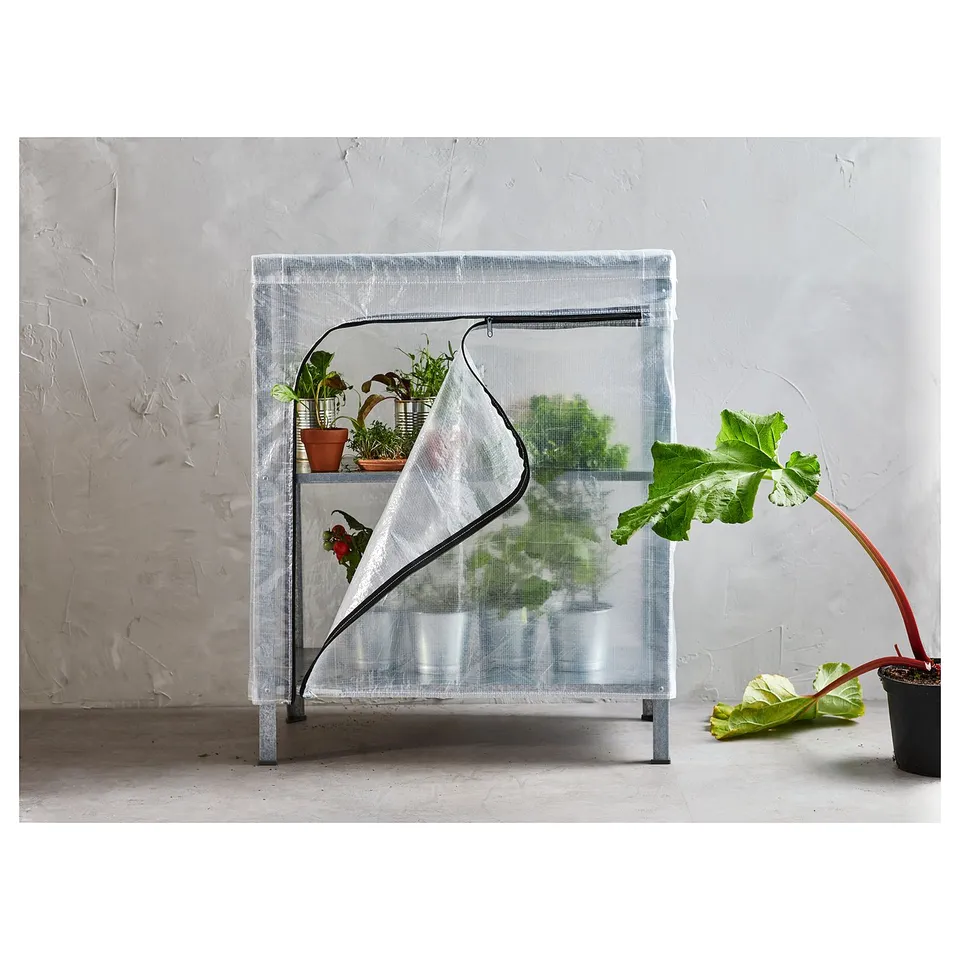 Small indoor greenhouse with potted plants, translucent cover, metal frame.