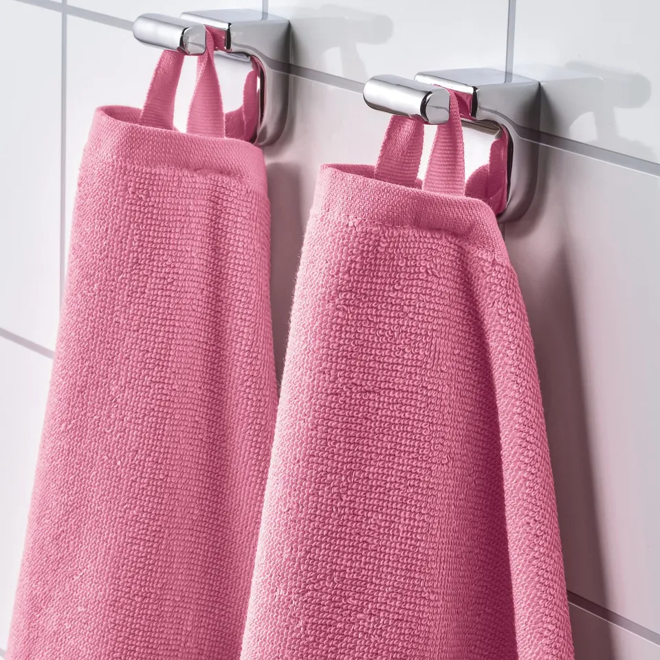 Two pink towels hang side by side on metal hooks, showcasing their absorbent and soft terry texture.