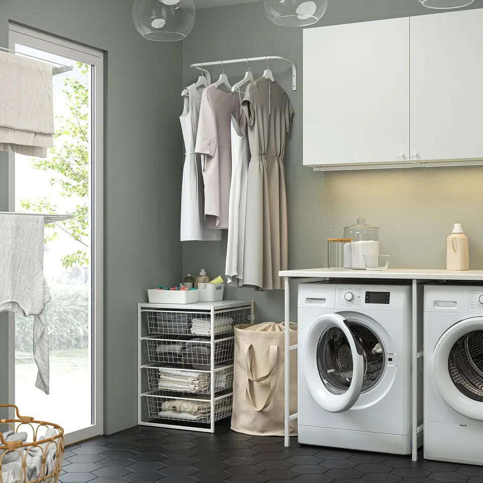 Modern laundry room with green walls, white shelves, cleaners, laundry bag, and washing machine.