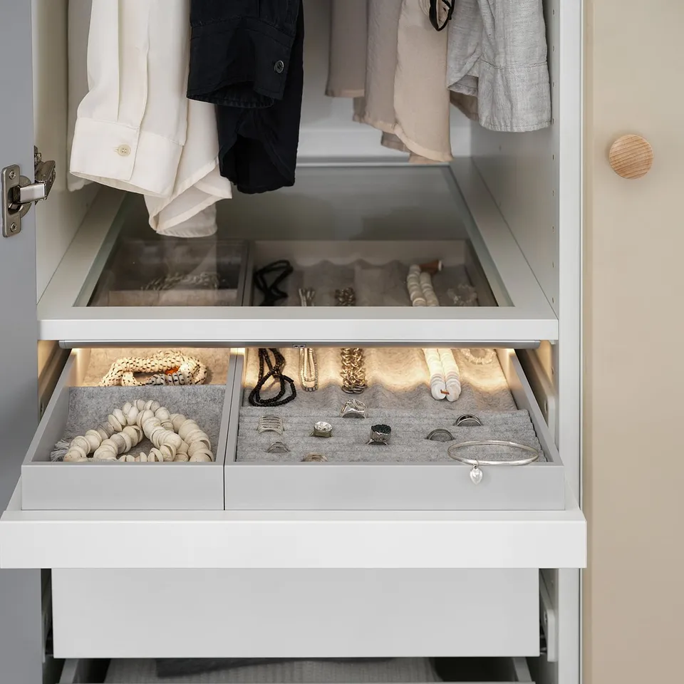 White wardrobe drawer with pull-out tray storing jewellery like necklaces, rings, and bracelets.
