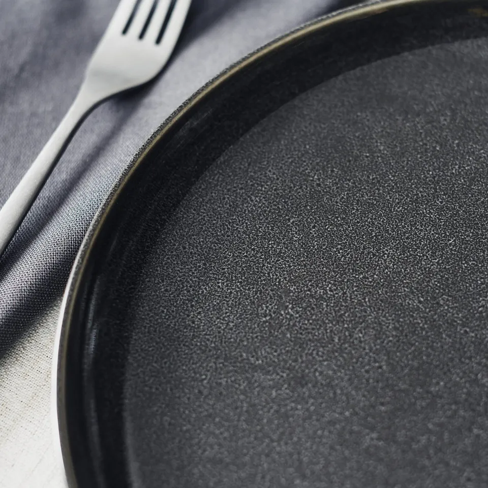Plate with fork, textured dark glaze, elegant setting.