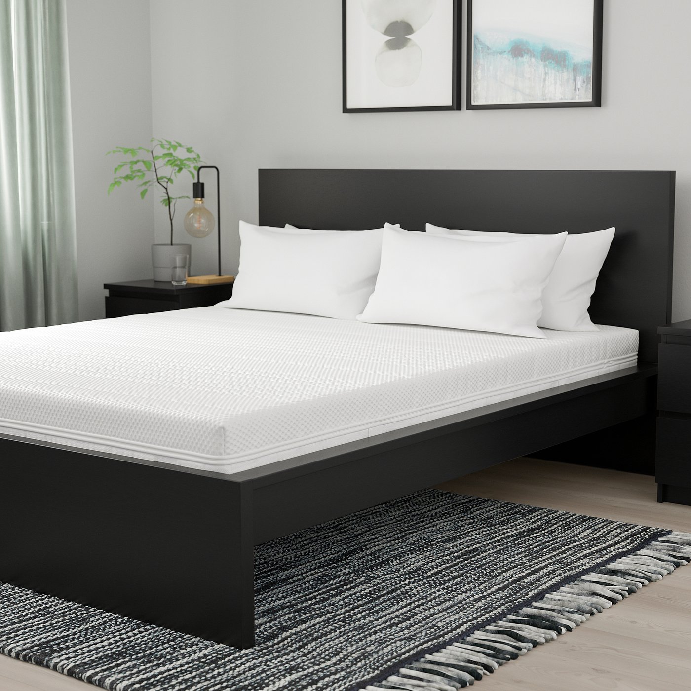Modern bedroom with black mattress, white bedding, plant, art, dark rug.
