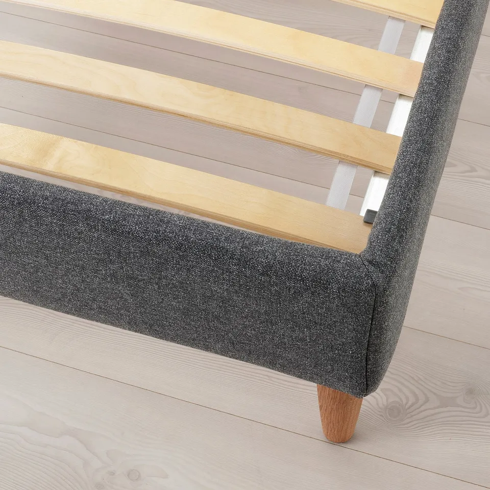 Modern bed with angled headrest, upholstered in grey. Wooden slats and turned legs. Ideal for comfort and style.