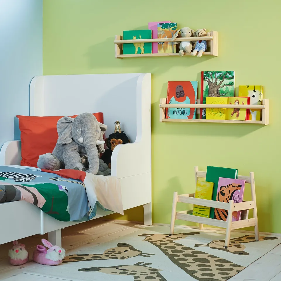 Childs room with colourful books, toys, and FLISAT shelves. Green & white walls, elephant bed.