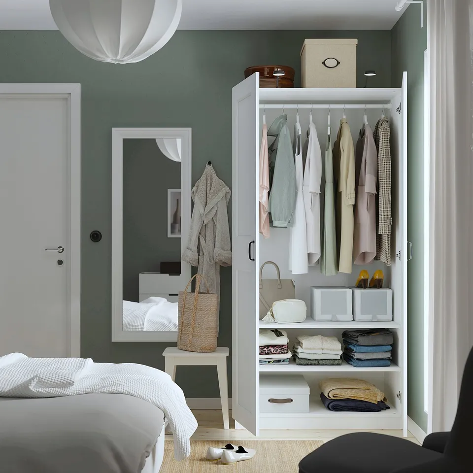 Bedroom with PAX wardrobe displaying clothes, accessories, and storage boxes. Mirror, bed, and pendant light also visible.