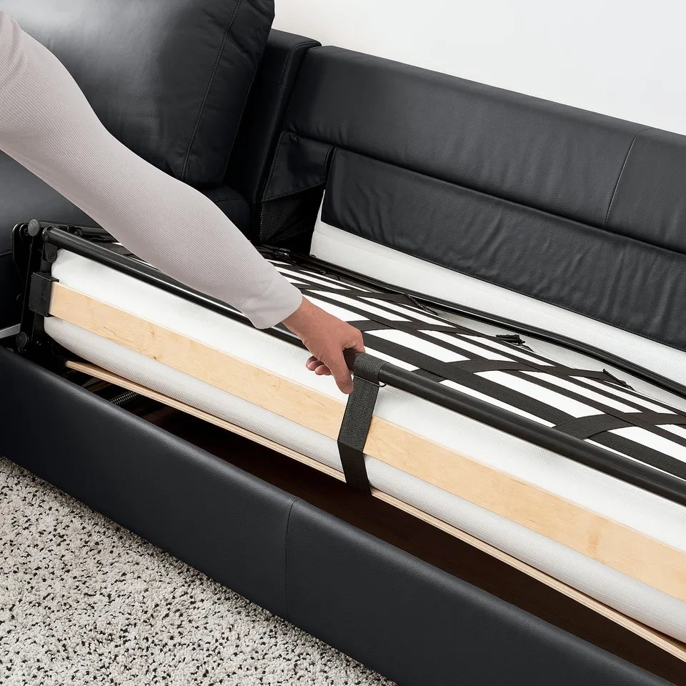 Person pulls up black sofa-beds mattress section. Easy-to-convert design, ideal for overnight guests.