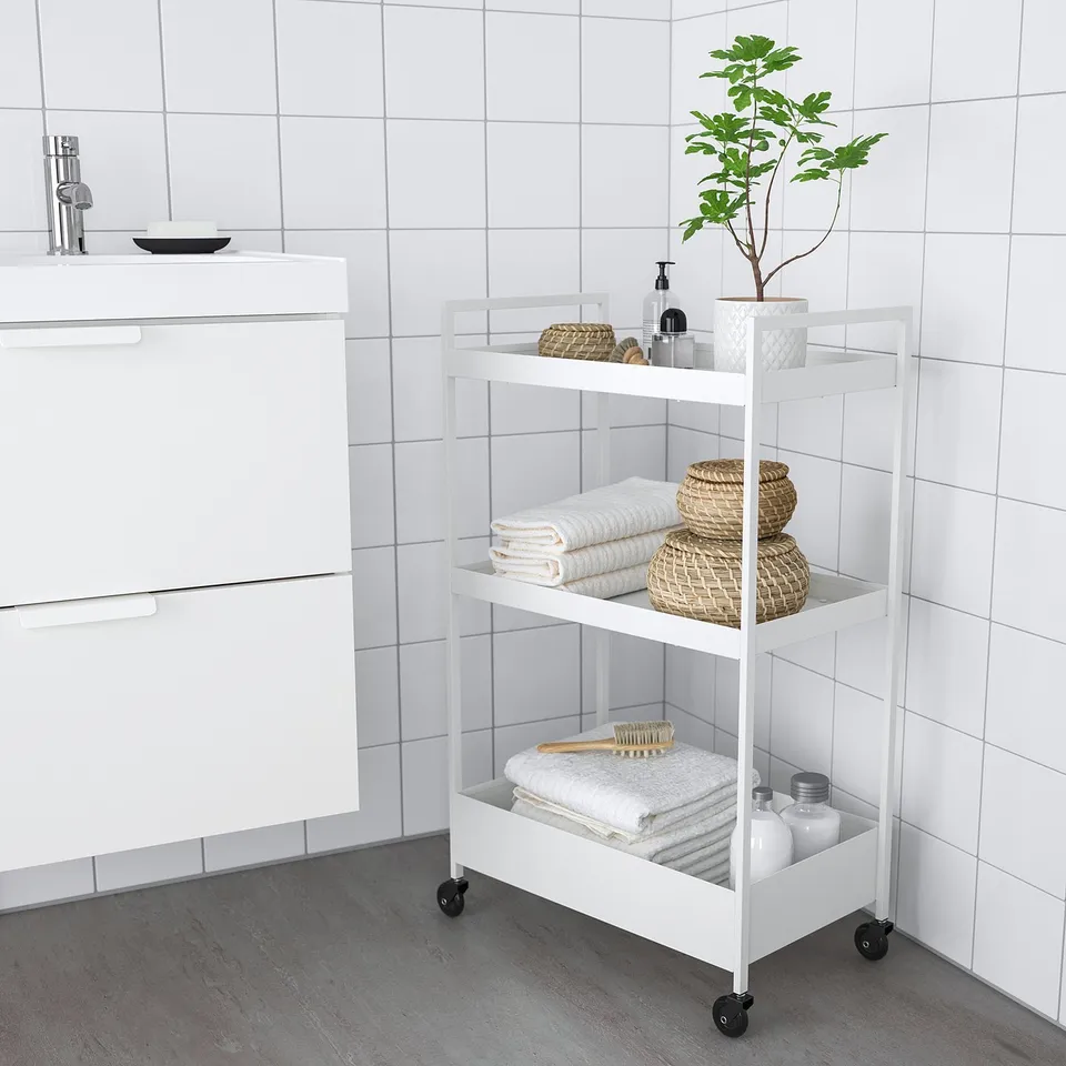 White NISSAFORS 3-tier rolling trolley, compact, with wicker baskets and folded towels for bathroom storage.