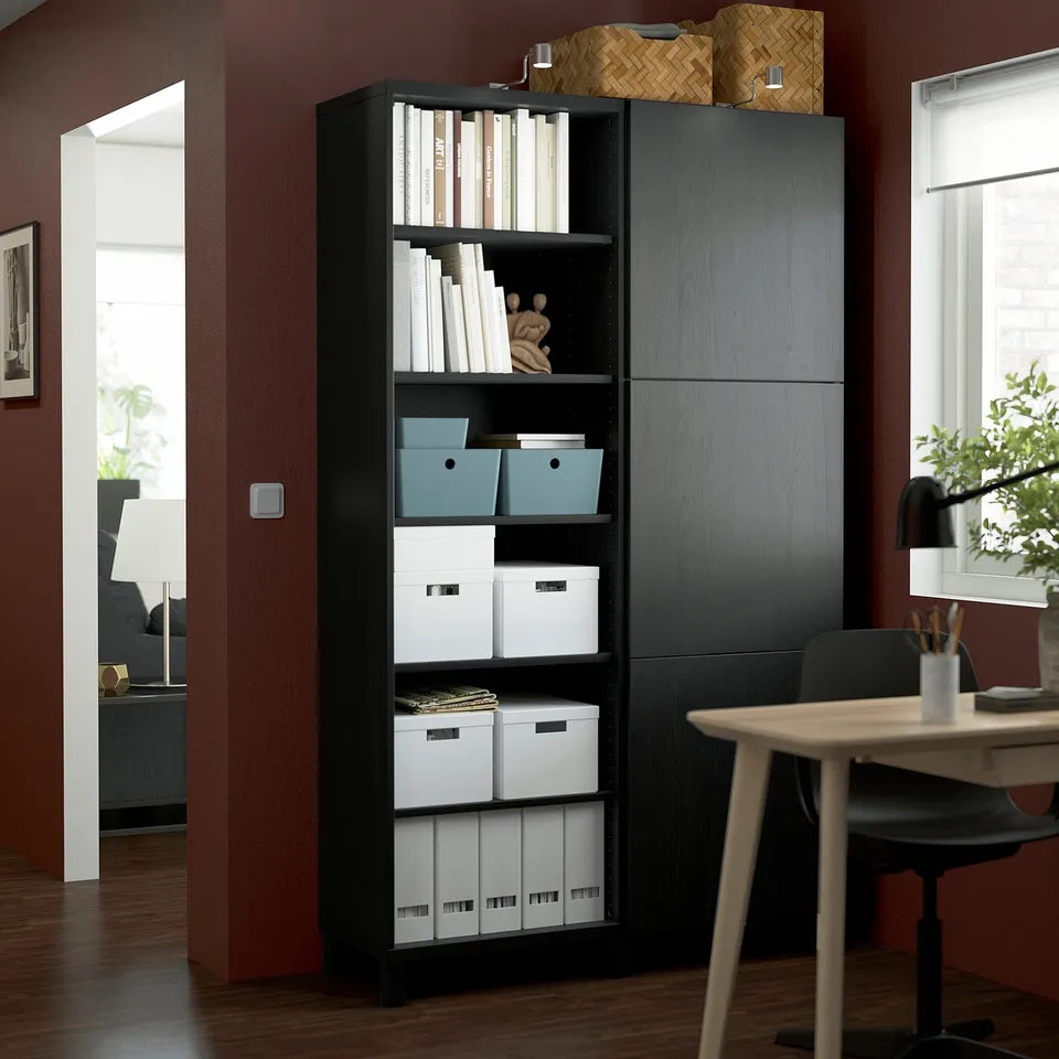 Black BESTÅ storage unit with shelves and cabinets near a door.