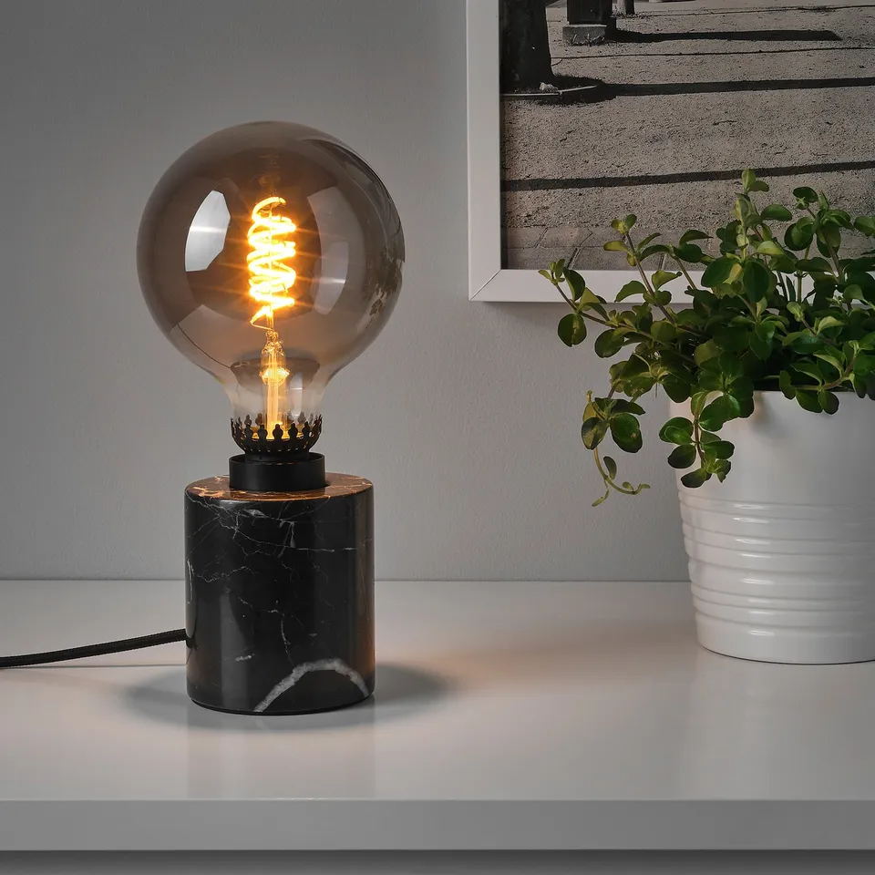 A small, modern table lamp with a black marble base and a warm, spiral led bulb on top, providing cosy mood lighting.
