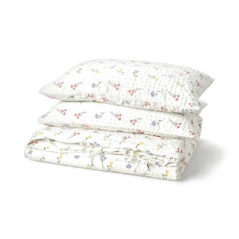 PILDVÄRGMAL duvet set, white with pastel flower prints, cotton/viscose blend, seersucker texture, folded neatly.