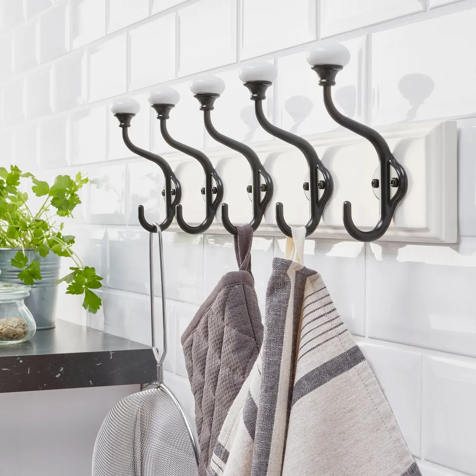 Four double black hooks mounted on a white wall hold towels and utensils. Simple and sturdy design for hanging items in two rows.