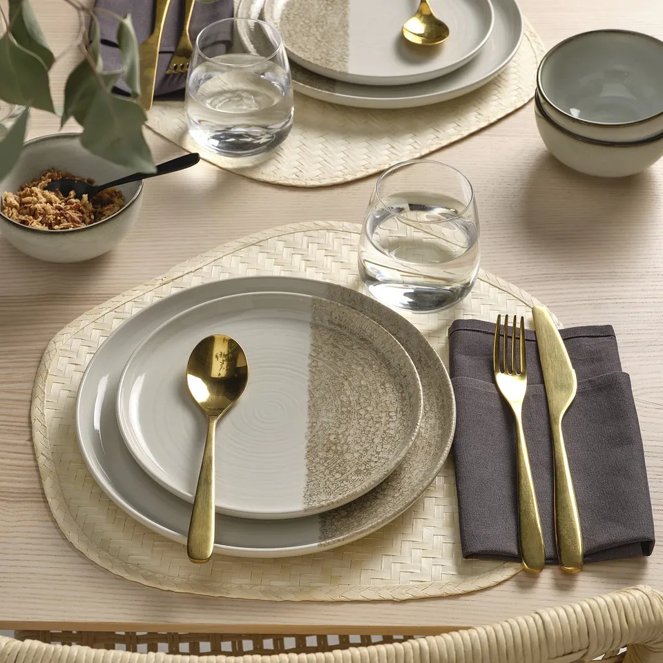 Elegant table setting with KRUSTISTEL plates, featuring colourful block designs and gold utensils, arranged on woven placemats.