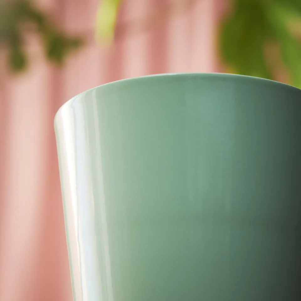 Close-up of smooth, glossy green pot, showing quality texture, against soft pink background.