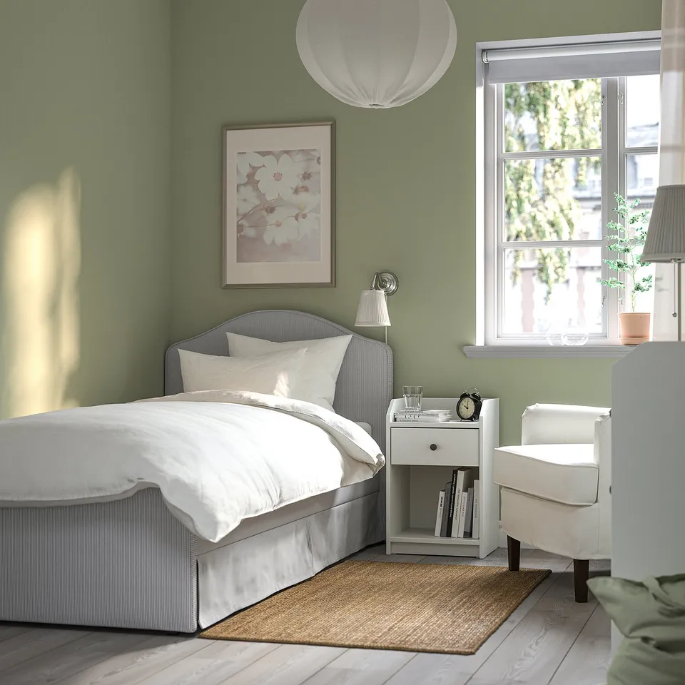 Green bedroom with RAMNEFJÄLL striped bed, white covers, bedside table, lamp, clock, and green view.