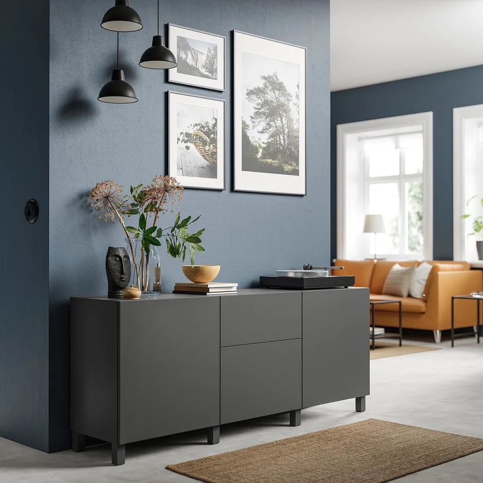 Modern living room with grey BESTÅ sideboard, black hanging lights, framed pictures, and orange sofa.