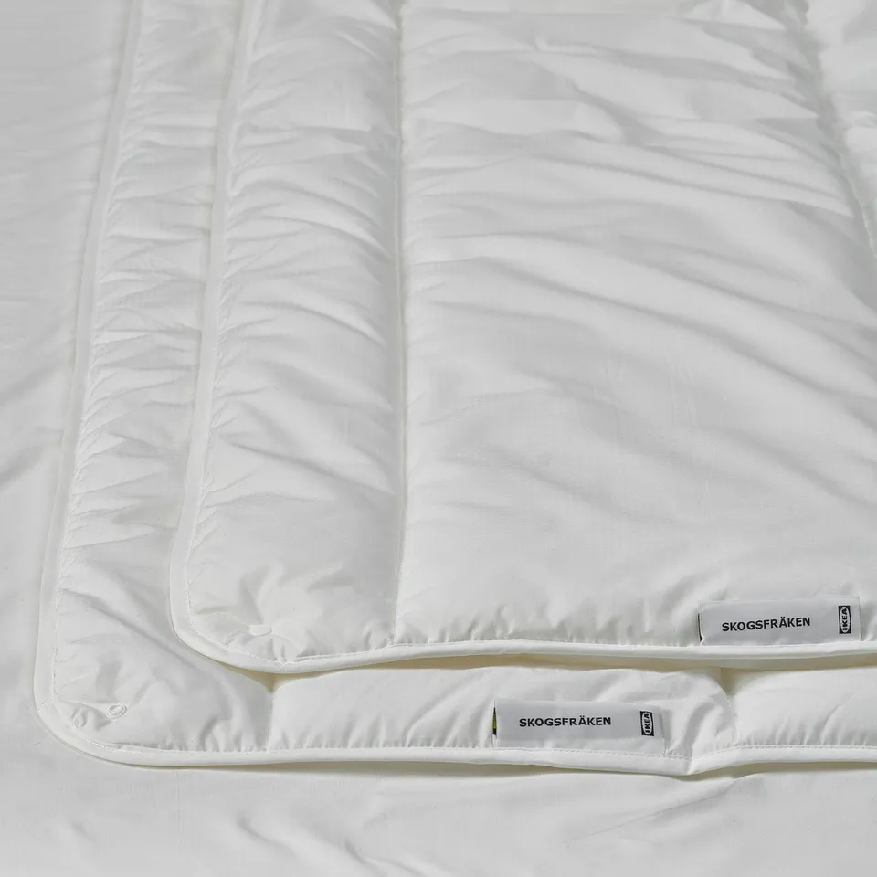 Clean, white duvet on bed showcasing quality fabric and craftsmanship, with visible brand tags SKOGSFRÄKEN and IKEA logo.