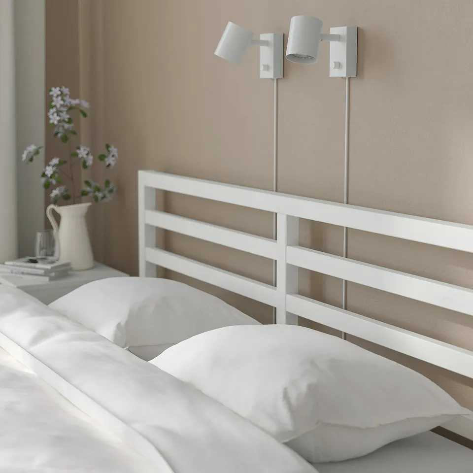Modern bedroom with white TARVA bed, two wall lamps, and a vase of flowers on a bedside table.