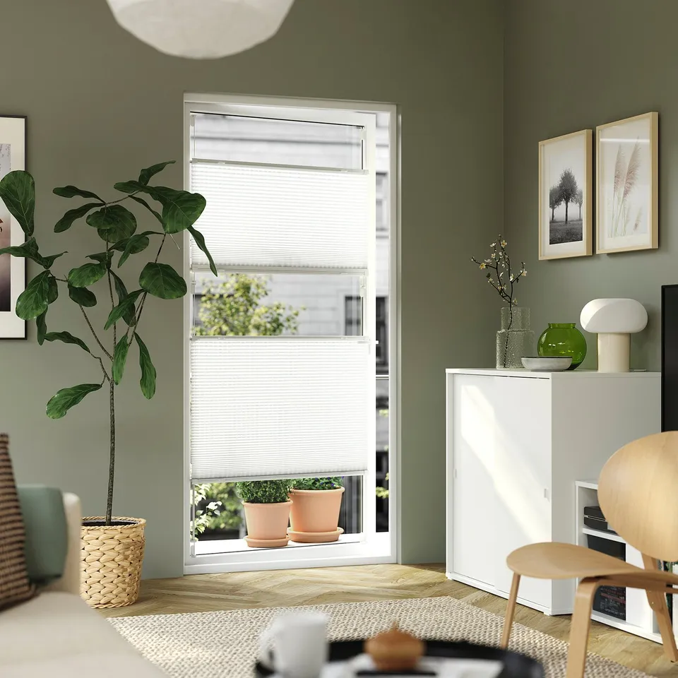 Room with green walls, HORNVALLMO white pleated blinds, plants, cabinet, chair, rug.