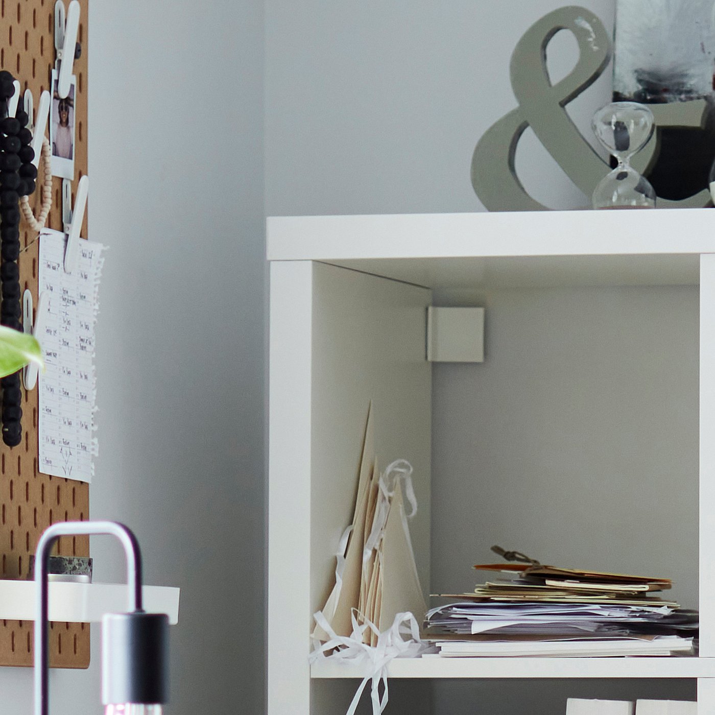 A grey ikea KALLAX shelving unit with white ribbons and papers neatly stacked on open shelves, using a pegboard for organization beside it.