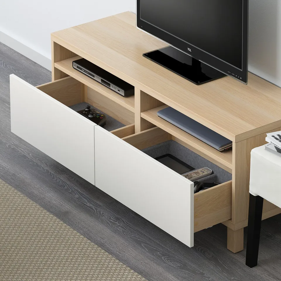 Light wooden tv stand with open drawer, showing cable management and storage for remotes and game controllers.