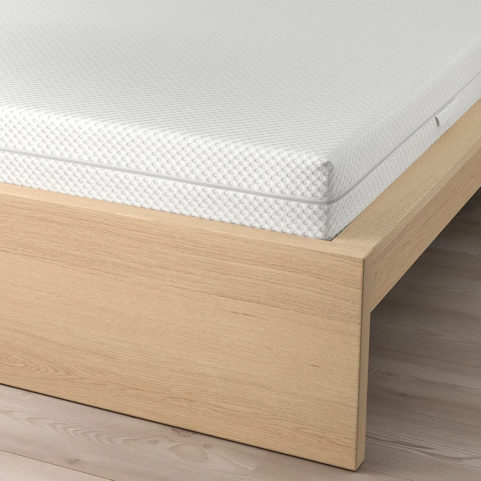 A bed with a white textured mattress on wooden slats, part of the MALM series, designed for comfort and support.