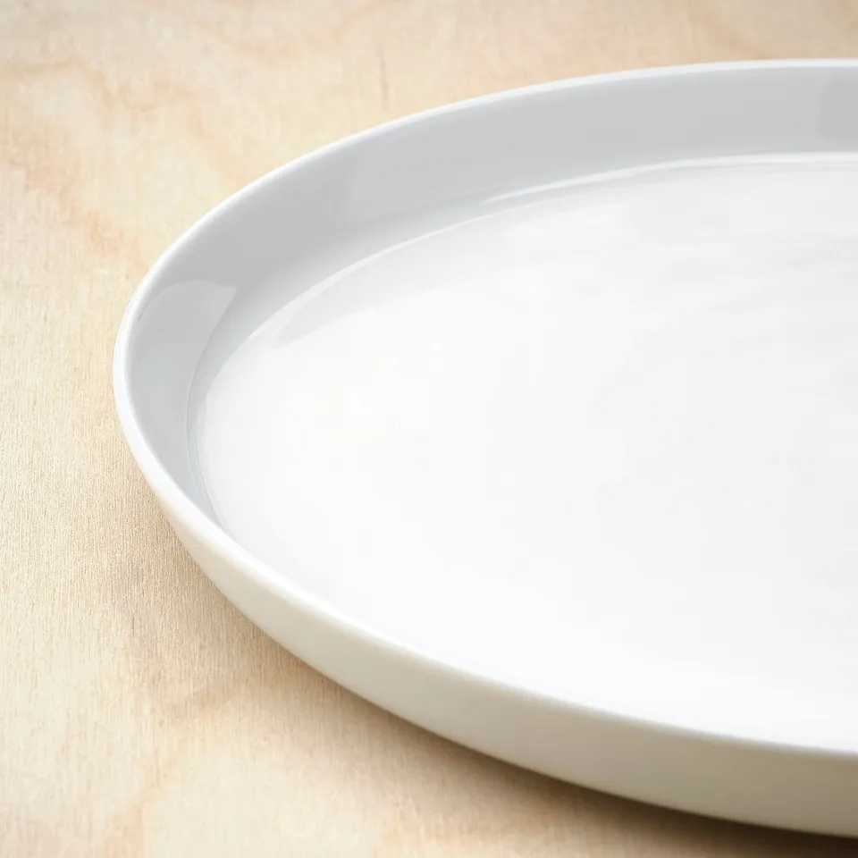 A pristine white porcelain dish on a wooden surface. The dishs smooth, even surface reflects light, showing its fine craftsmanship and quality.