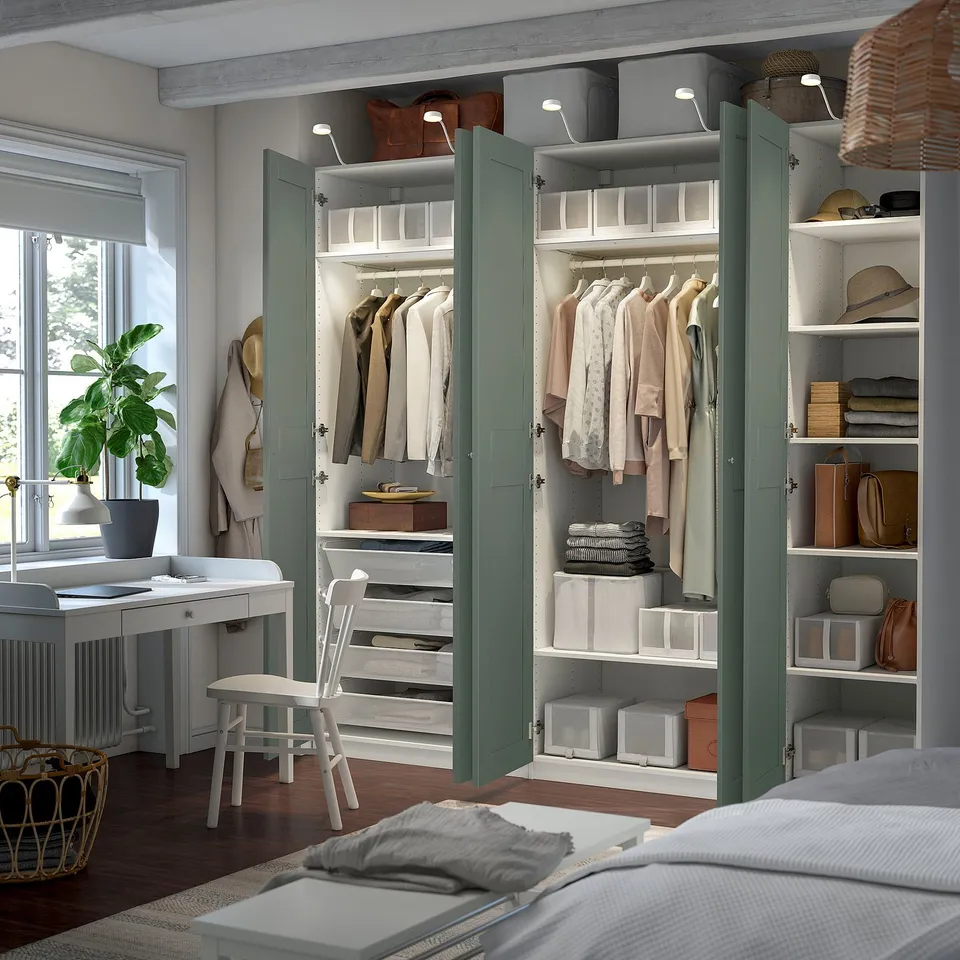 Modern bedroom with open PAX wardrobe showing clothes hangers, shelves, and storage boxes, highlighting organised storage space.