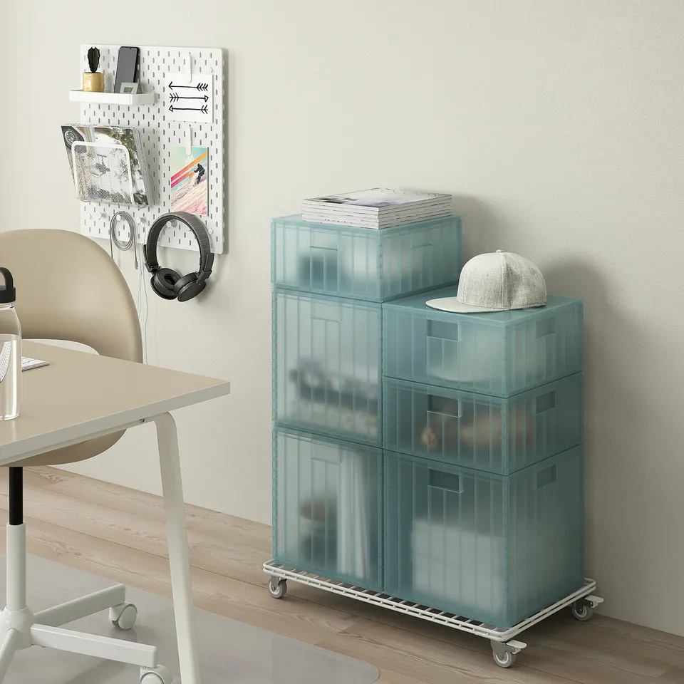 Slim, blue INVALLNING storage trolley fits under white desk, with wheels, holds light cap.