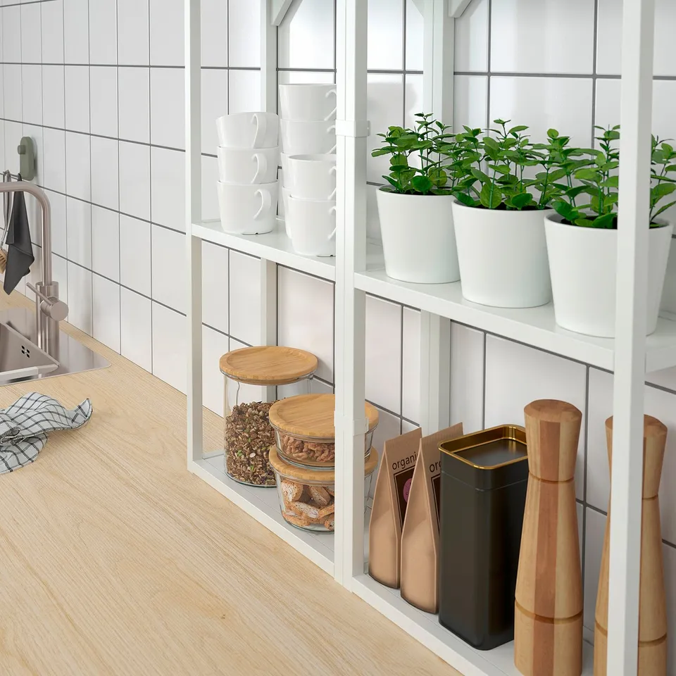 Modern kitchen shelf with white SOJABÖNA pots holding green plants, wood lids, and bowls; nearby sink and countertop.