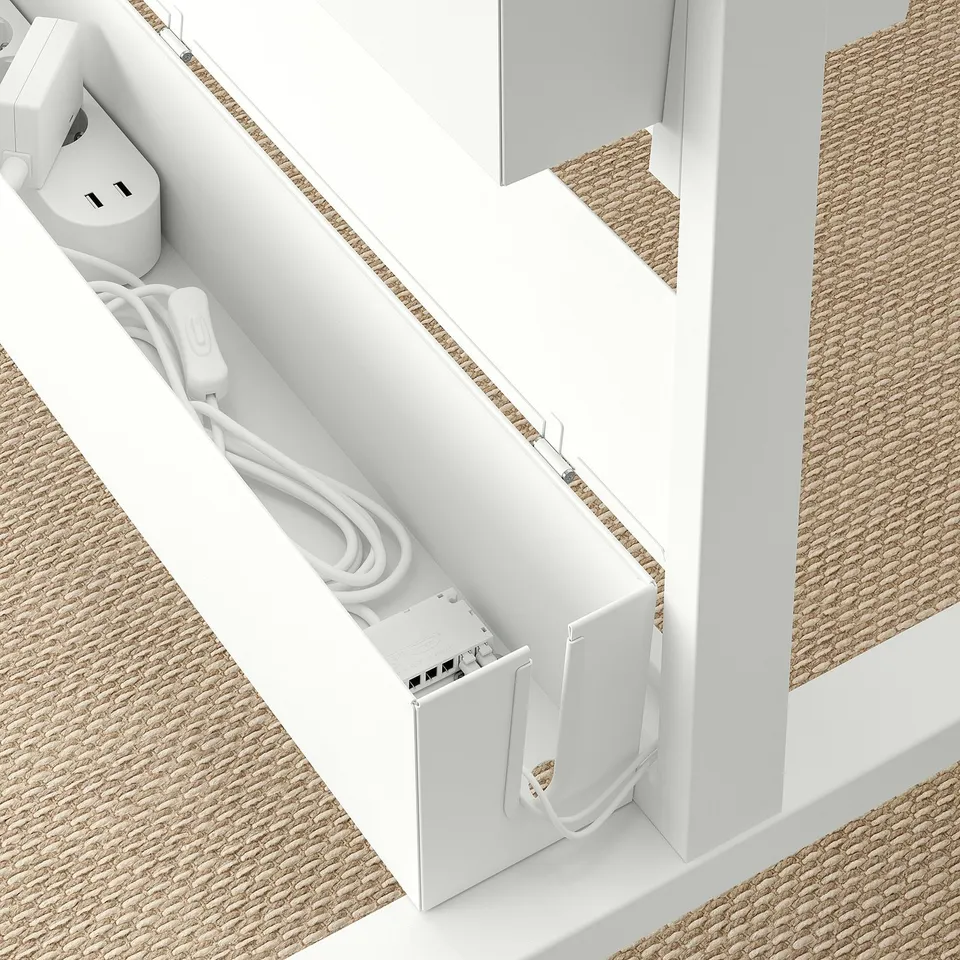 White cable box with open door displaying connectors and coiled cables next to desk on beige floor.