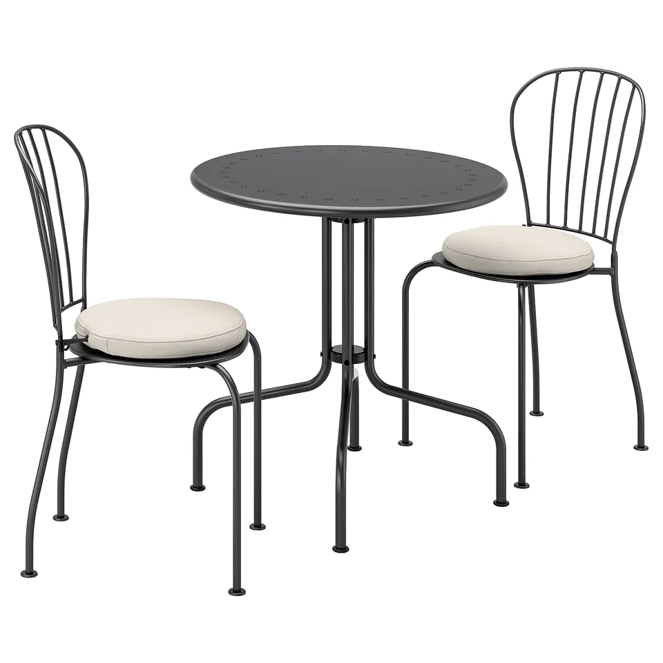 A black LÄCKÖ outdoor patio set with a round table and two chairs. The chairs have beige cushions and curved backs.