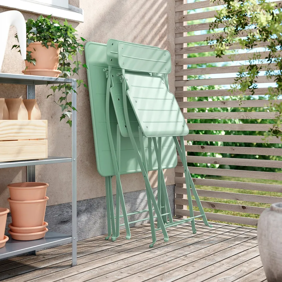 Two green SUNDSÖ folding chairs leaned against fence on balcony.