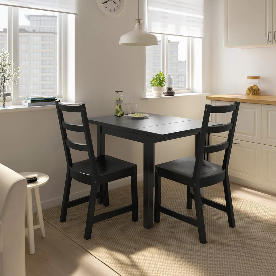 Small black, foldable NORDVIKEN dining set with table and two chairs in a bright room.
