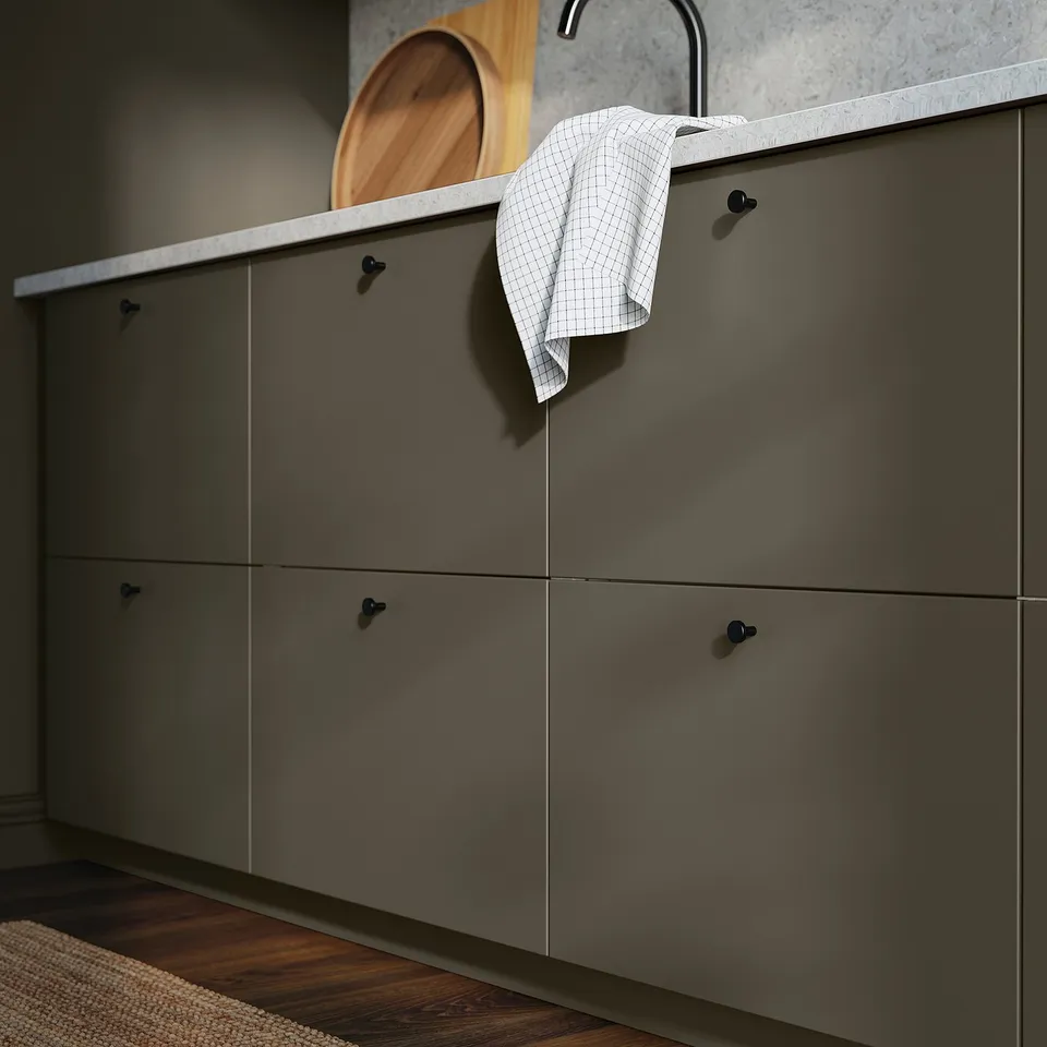 A grey HAVSTORP storage cabinet with dark knobs, hanging towel, and wooden floor.