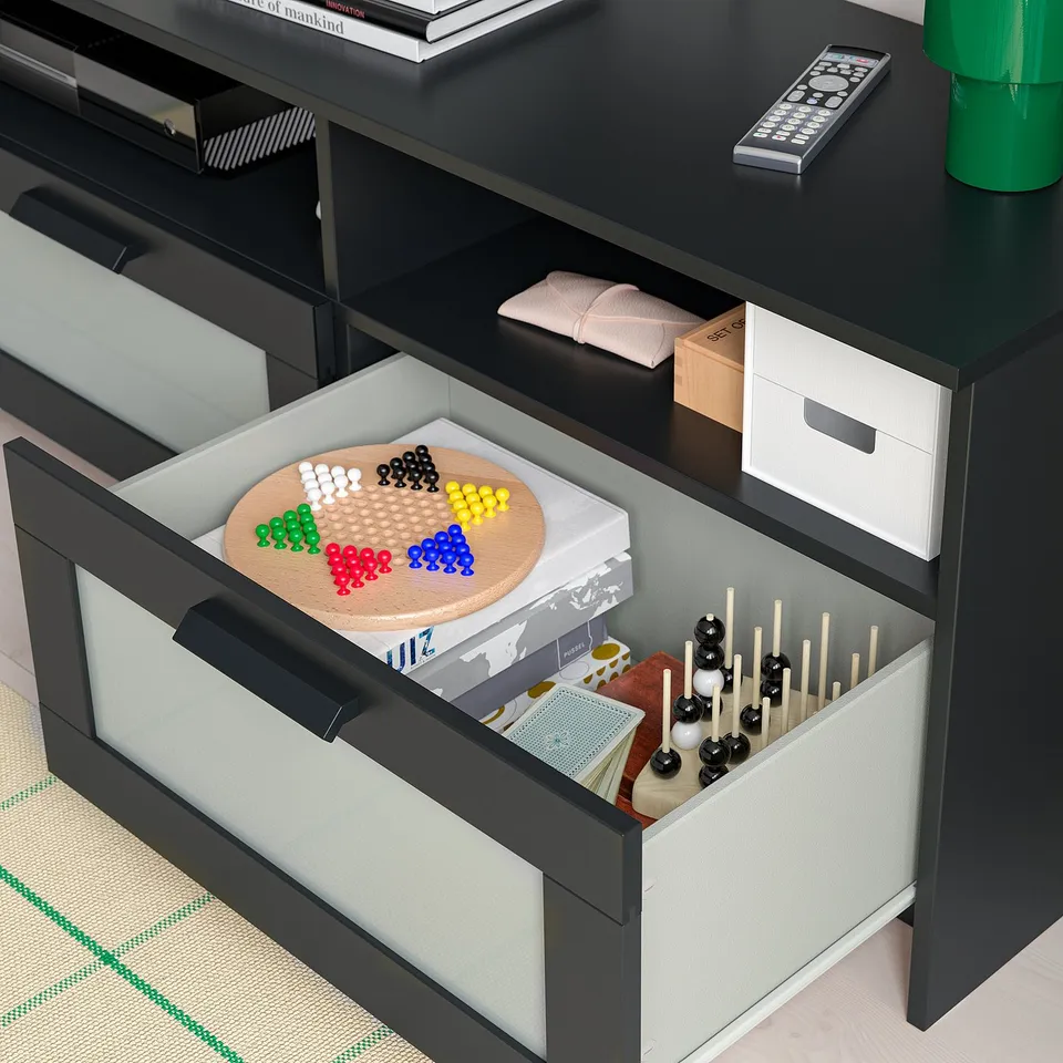 Black tv stand with open drawer showing games, remote, and boxes. Drawers hide cables, organise media accessories.