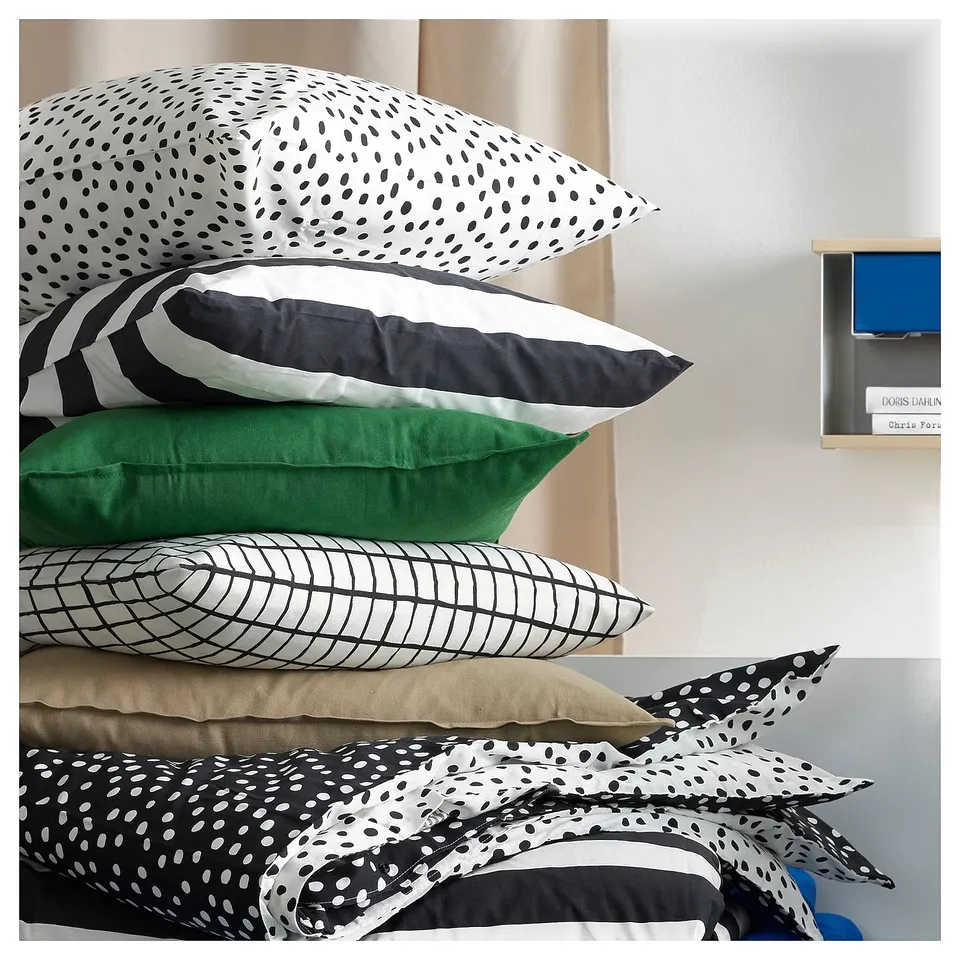 Pile of multicoloured pillows, including black and white striped, green, and grid-patterned ones on a bed.