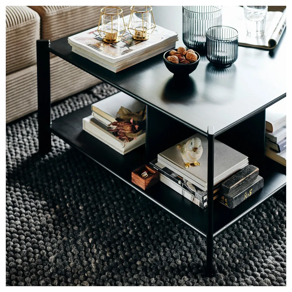 Black coffee table with bamboo shelves, metal legs, books, and decor items.